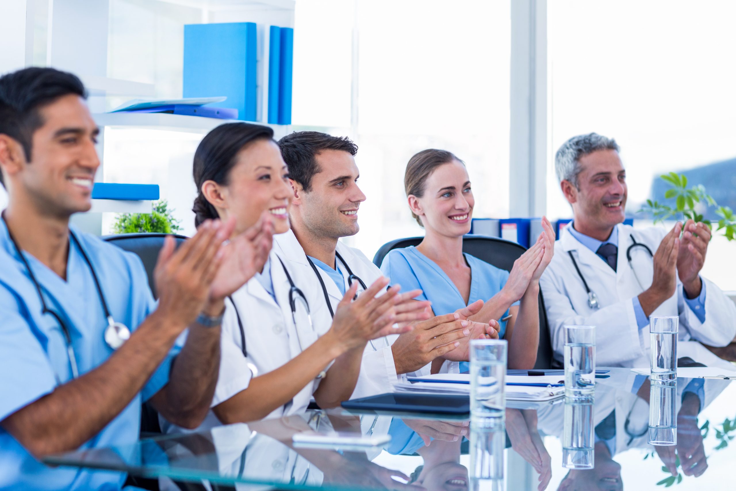 doctors applauding while sitting table scaled